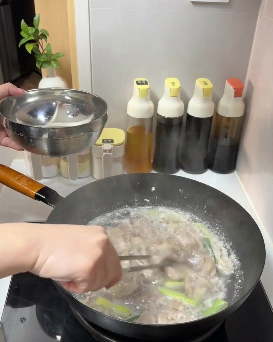 Fettine di manzo cotte sollevate da una pentola di acqua bollente con le pinze e trasferite in una ciotola di metallo.