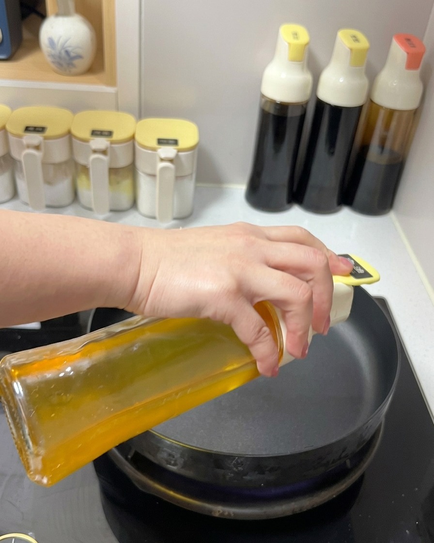 Olio di semi limpido versato da un oliatore di vetro in una padella nera sul fuoco.