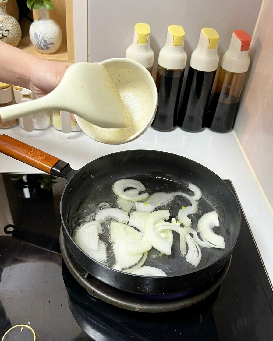 Fettine di cipolla bianca saltate in padella con olio usando una spatola bianca.