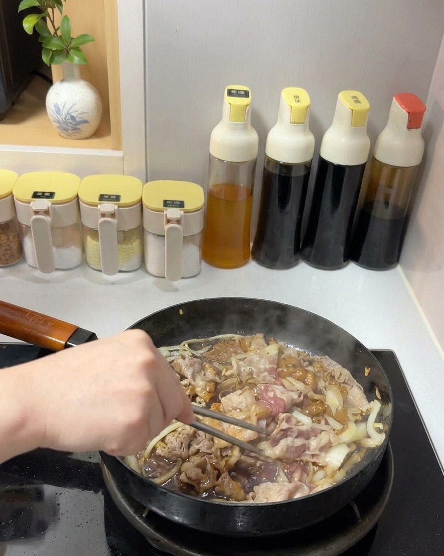 Manzo e cipolle saltati con una salsa scura e lucida in padella usando bacchette di metallo.