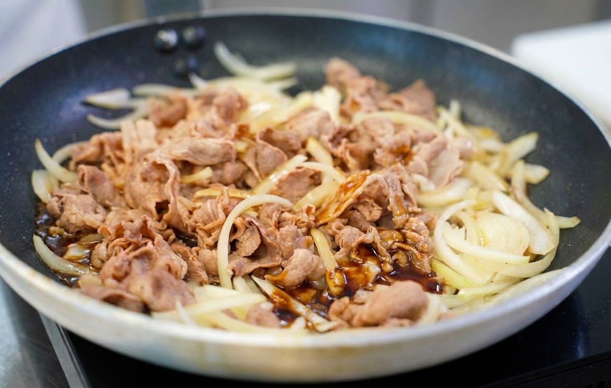 Una salsa saporita, densa e marrone scuro viene versata su un mix di manzo e cipolle saltate in padella.