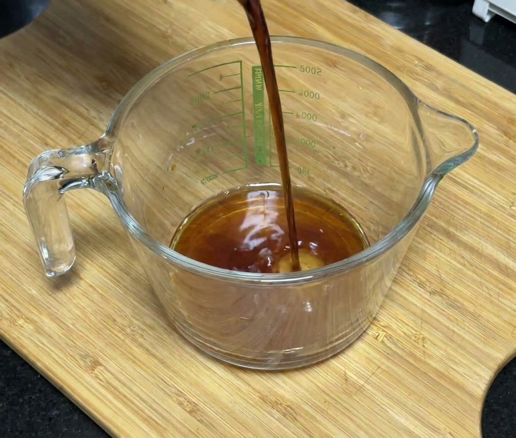 Salsa di soia scura versata in un misurino di vetro contenente miele e aromi.