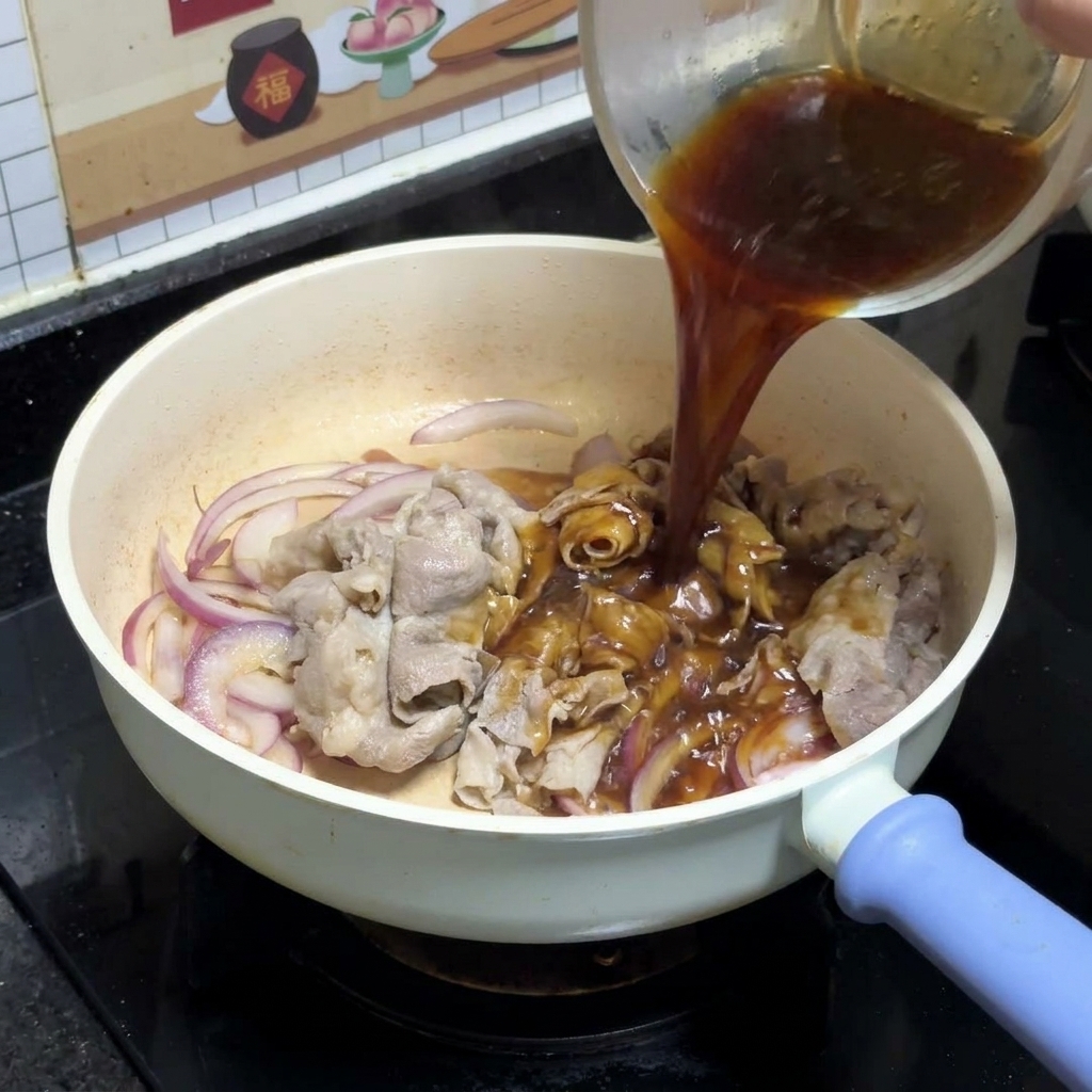Salsa teriyaki scura versata da una ciotola di vetro trasparente sopra le cipolle rosse saltate e le fettine di manzo in una padella bianca.