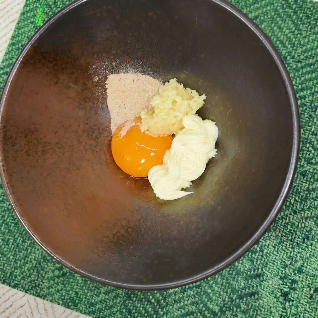 Polvere di condimento per ramen versata sopra un tuorlo duovo, maionese e aglio in una ciotola.