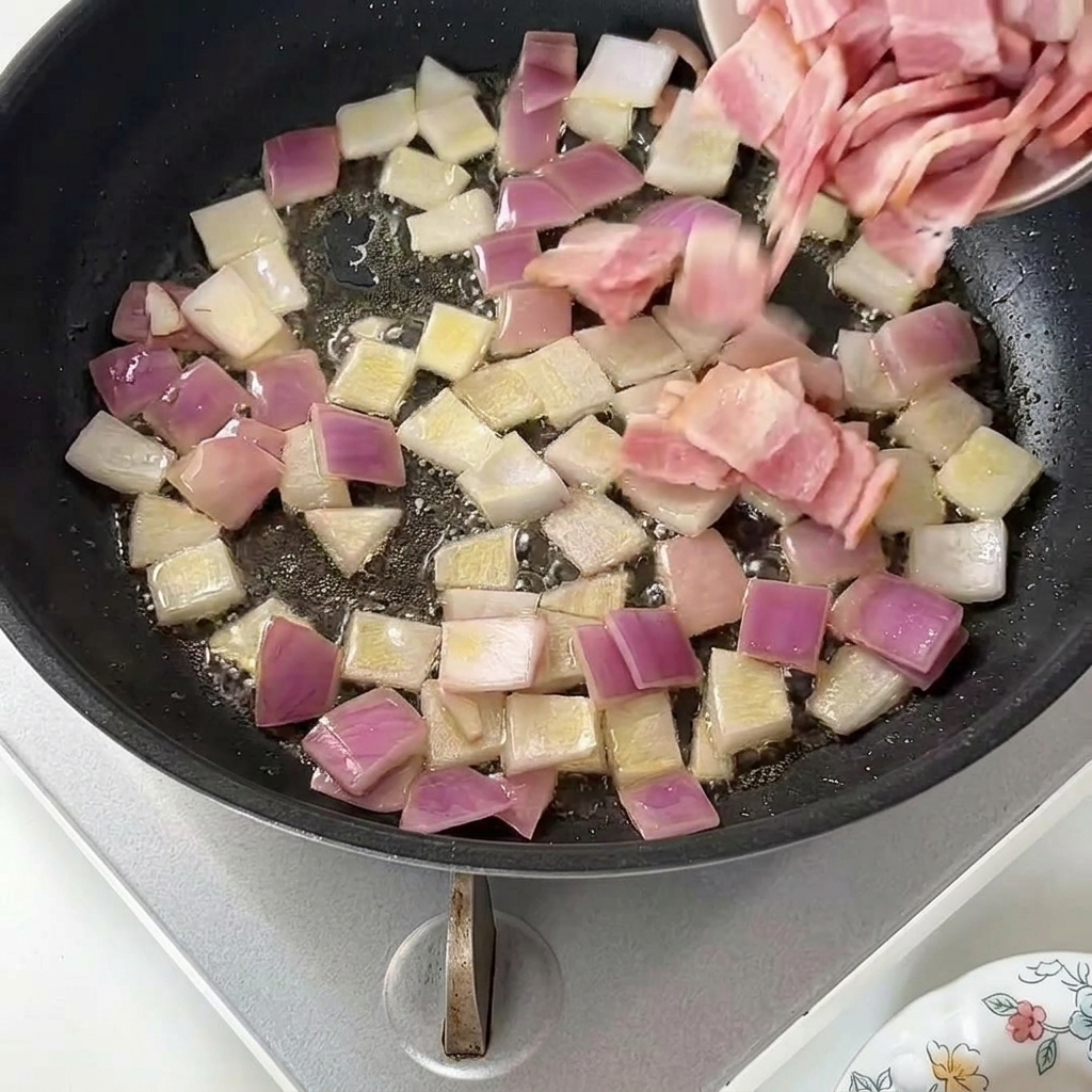 Aggiunta di pezzetti di bacon crudo da un piattino in una padella con cipolla rossa soffritta.