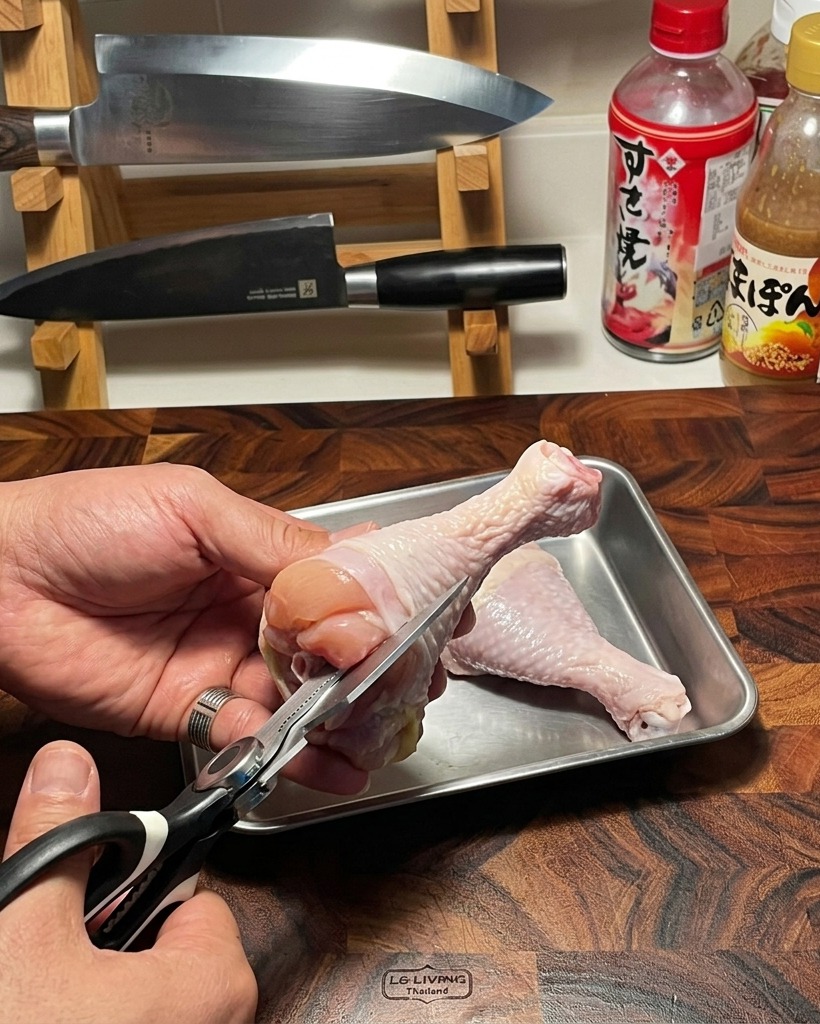 Un paio di forbici da cucina utilizzate per rimuovere con cura losso da una coscia di pollo cruda su un tagliere di legno.