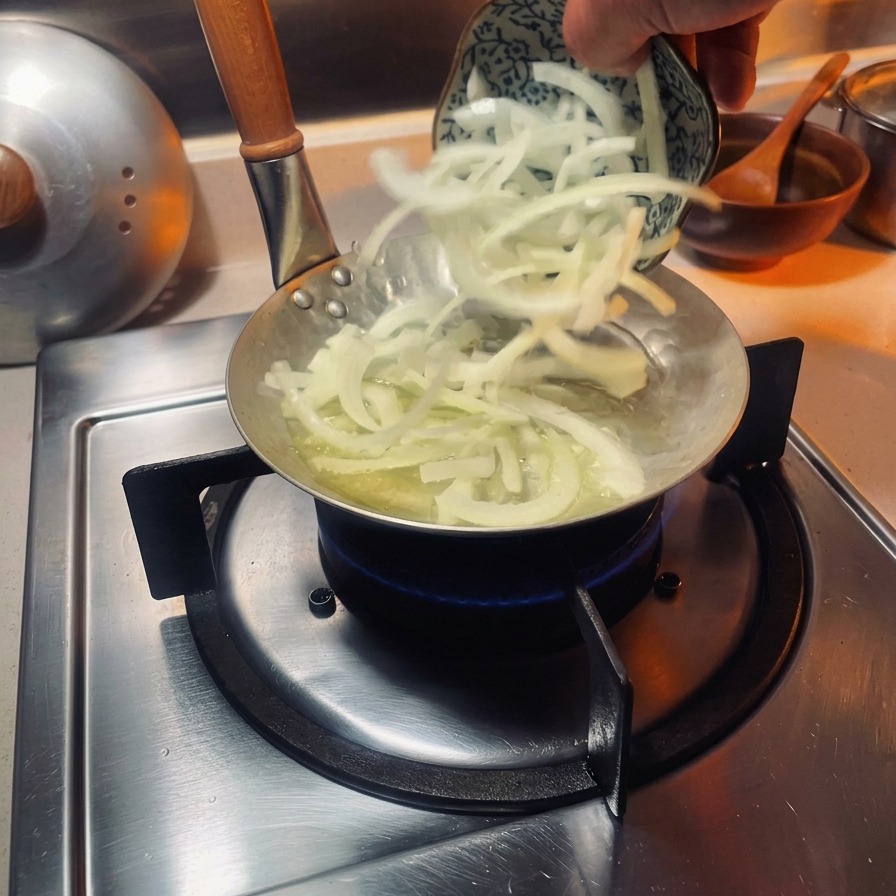 Cipolle bianche affettate che vengono aggiunte in una piccola padella specifica per oyakodon su un fornello a gas.
