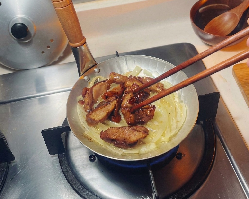 Pezzi di pollo scottati disposti con le bacchette su un letto di cipolle traslucide in una piccola padella.