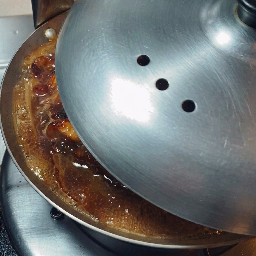 Un coperchio di metallo lucido posizionato sopra una padella bassa per trattenere il vapore e far sobbollire il contenuto.