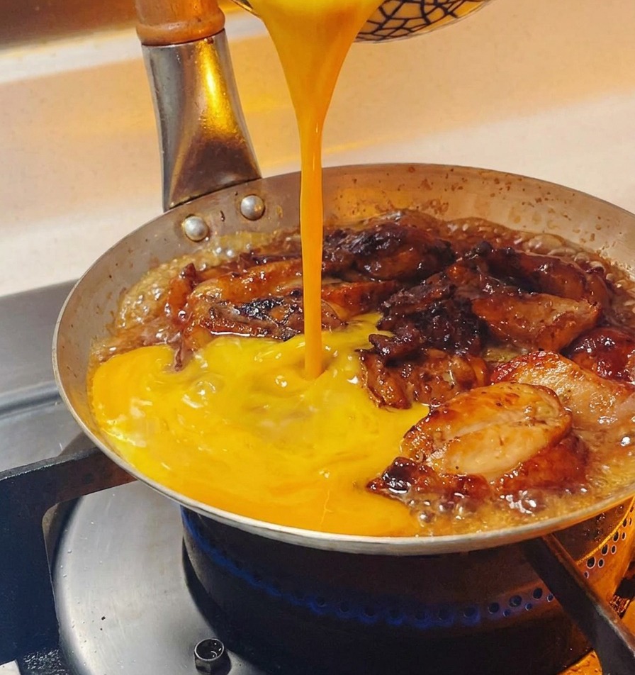Uovo sbattuto giallo-dorato versato con un movimento circolare in una padella sopra i pezzi di pollo in umido.