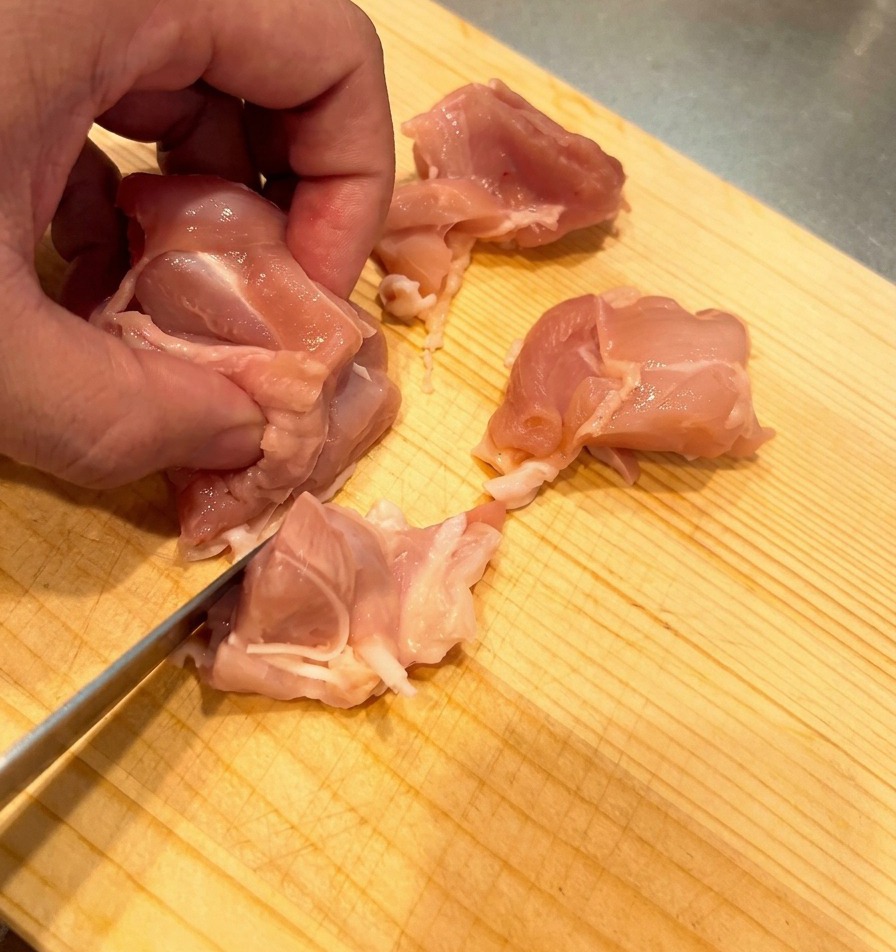 Pollo crudo tagliato a bocconcini uniformi su un tagliere di legno chiaro.