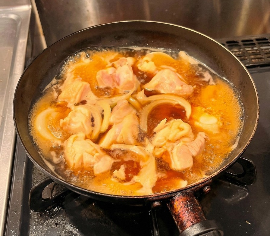 Uova sbattute versate a filo sopra il pollo e le cipolle che sobbollono in una padella nera.