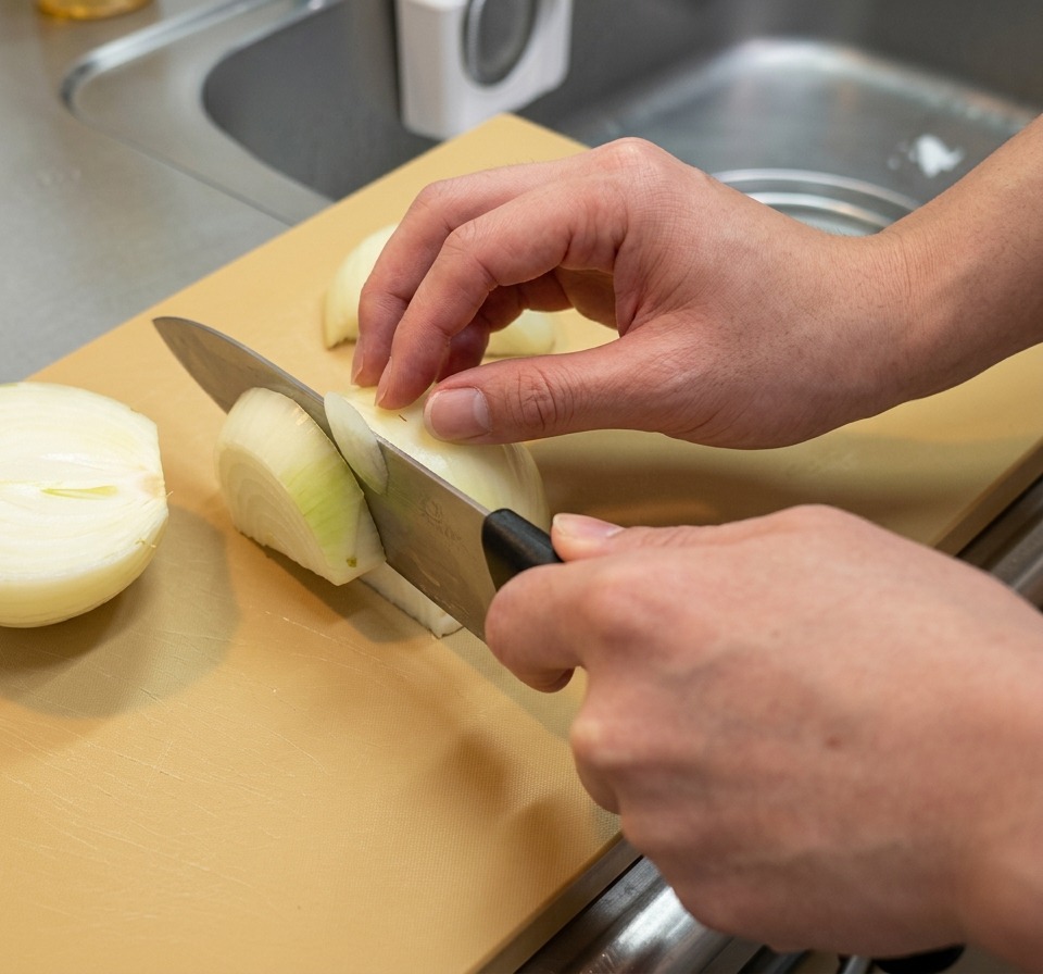 Metà di cipolla tagliate a spicchi longitudinali spessi su un tagliere marrone chiaro.