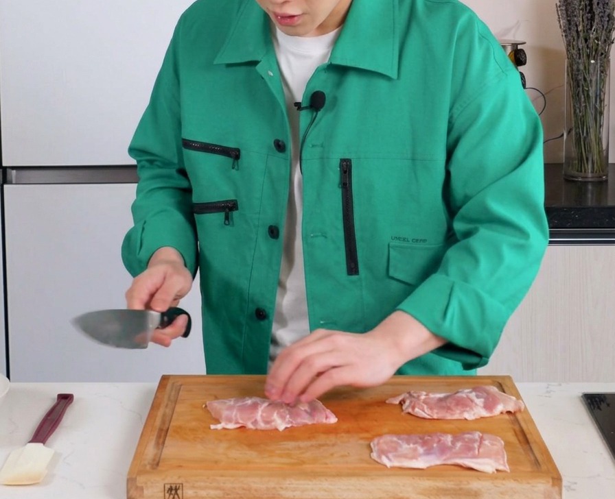 Un coltello che pratica lievi incisioni sulla carne di sovracosce di pollo disossate su un tagliere di legno.