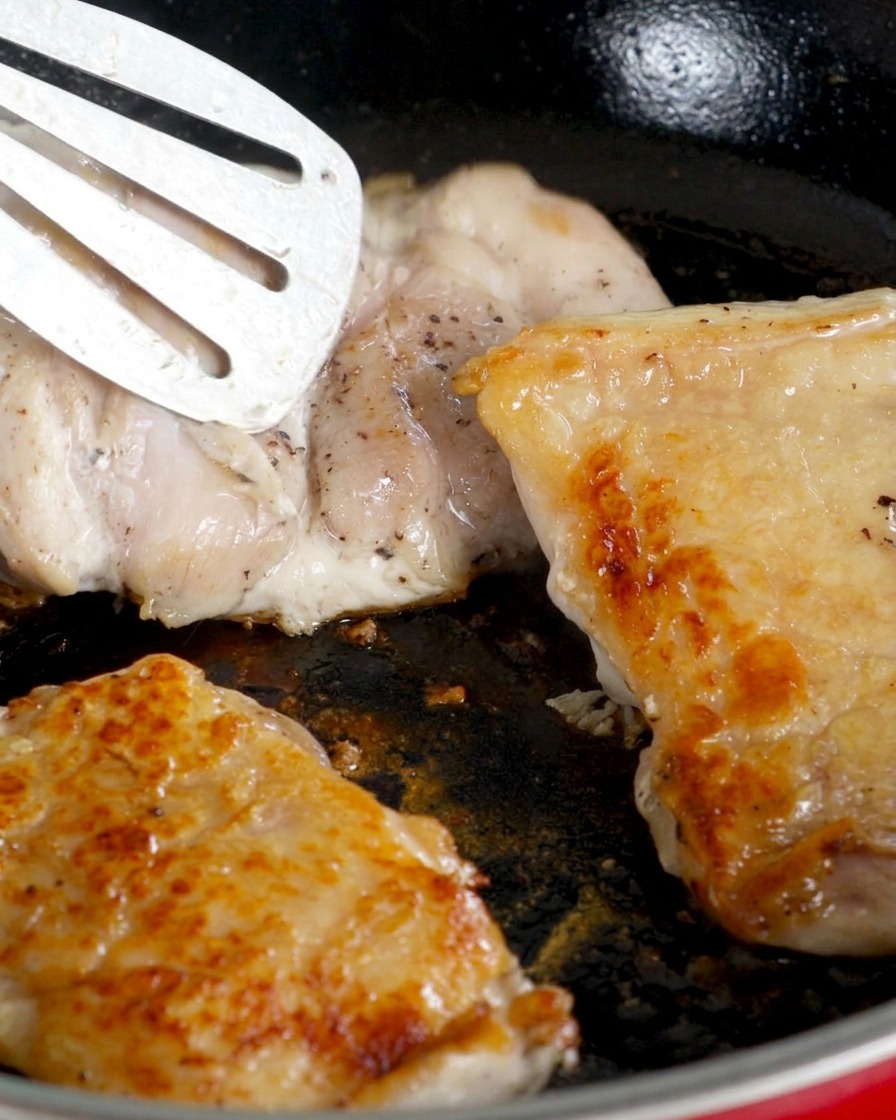 Cosce di pollo girate in padella con la pelle dorata rivolta verso lalto mentre cuoce il lato della carne.