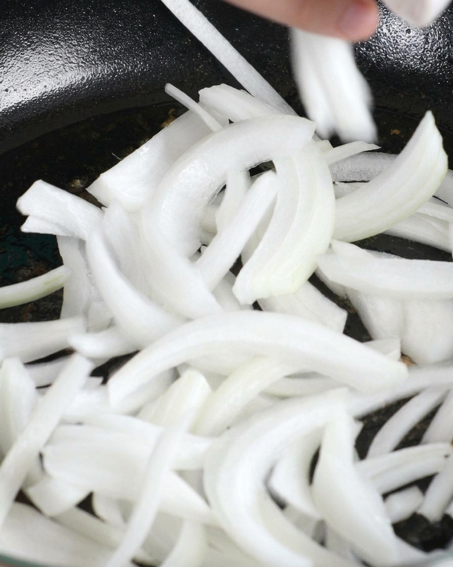 Cipolle bianche affettate che vengono versate nella padella con il grasso del pollo.