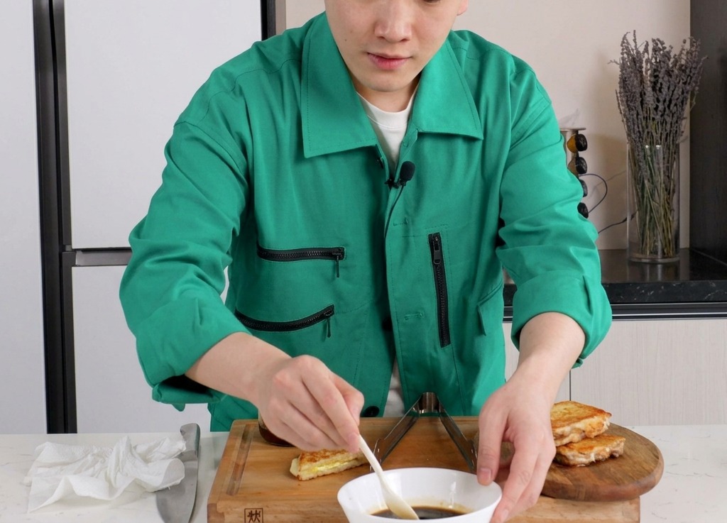 Una persona che mescola una salsa scura a base di soia in una ciotola di ceramica bianca con un cucchiaino.
