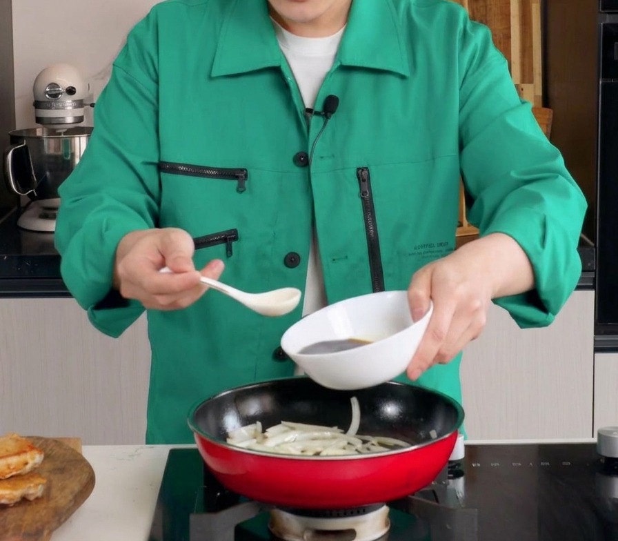Salsa scura e saporita versata da una ciotola bianca in una padella rossa con le cipolle appassite.