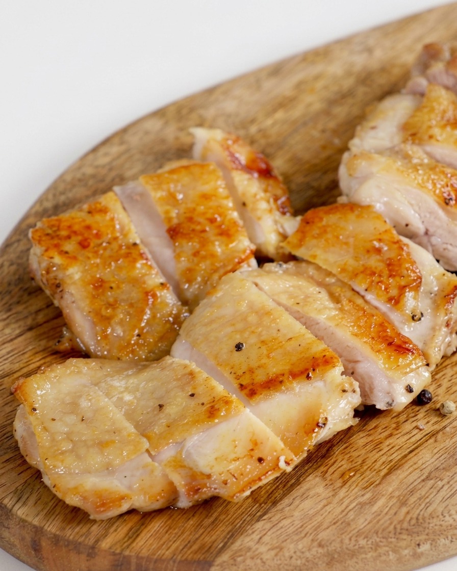 Coscia di pollo dorata in padella e tagliata in striscioline uniformi su un tagliere di legno.