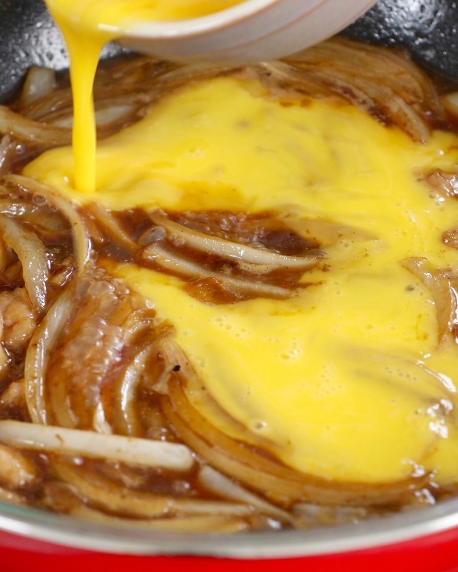 Uova sbattute dorate versate da una ciotola in una padella con cipolle e salsa di soia scura.