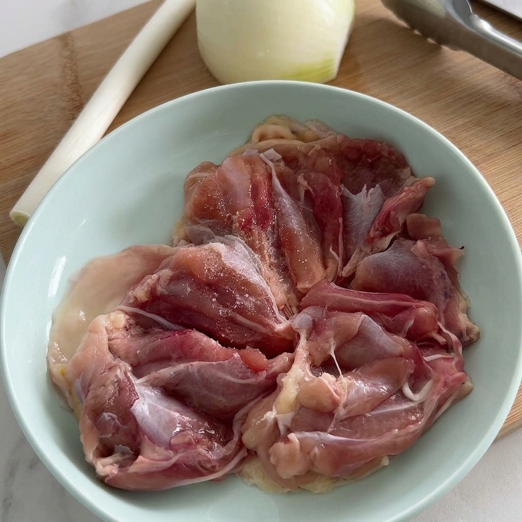 Filetti di sovracoscia di pollo cruda in una ciotola azzurra, conditi con sale e pepe nero macinato fresco.