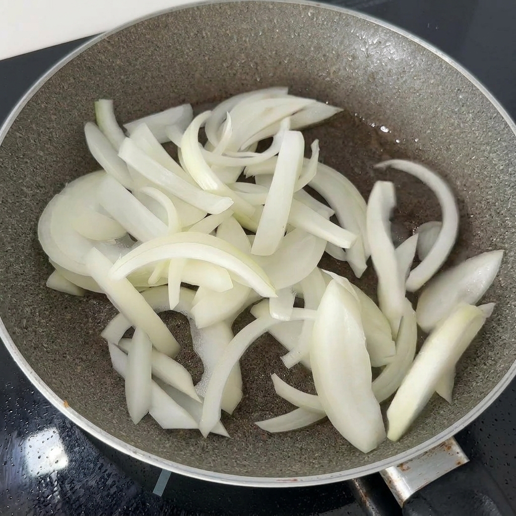 Cipolle bianche affettate sottilmente fatte saltare in una padella scura con il grasso residuo del pollo fino a diventare morbide.