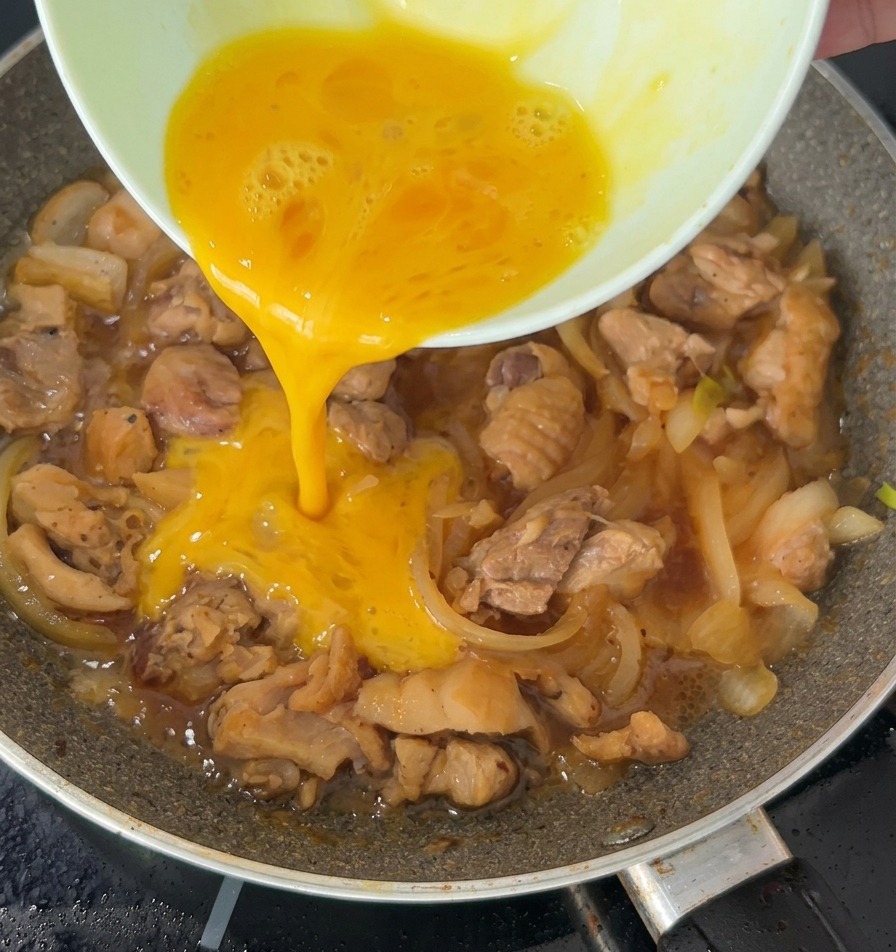 Uovo sbattuto versato a filo sopra il pollo e le cipolle che sobbollono in padella.