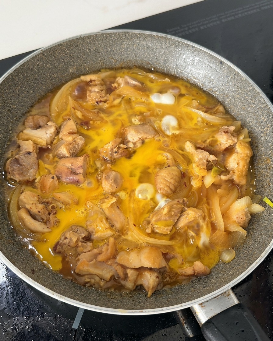 Composto di uova parzialmente cotto che sobbolle in padella con pezzi di pollo e cipolle affettate nel brodo di soia.