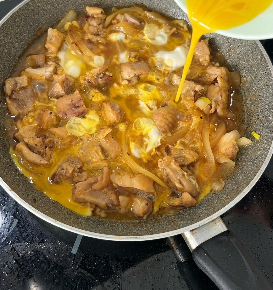 La seconda metà del composto di uova sbattute versata sopra un Oyakodon quasi ultimato in padella.