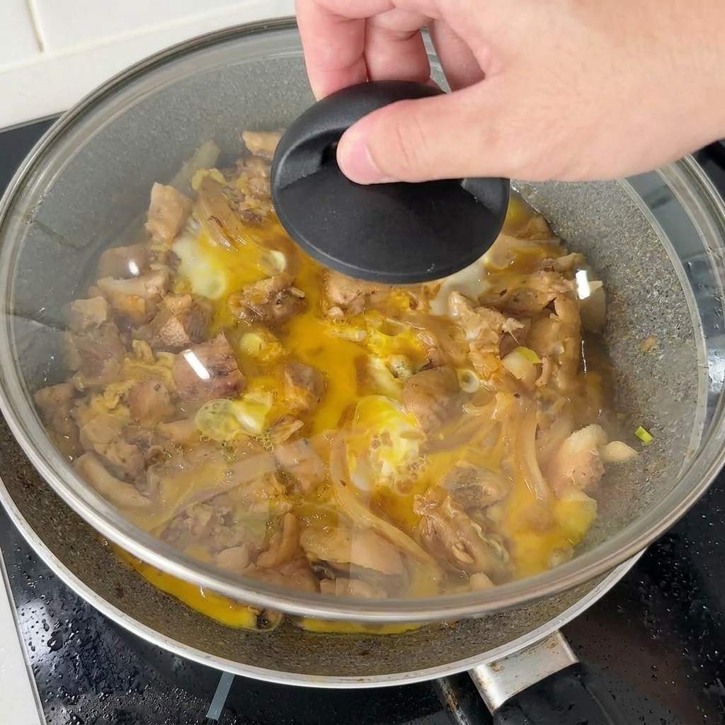 Una mano che posiziona un coperchio di vetro su una padella con pollo e uova per far rapprendere lultimo strato con il vapore.