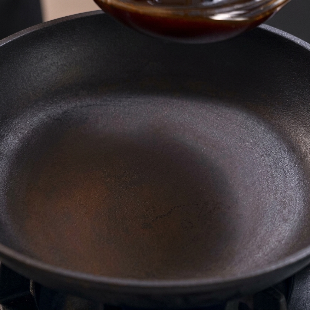 Una salsa per Oyakodon scura e agrodolce viene versata in una padella nera su un fornello.