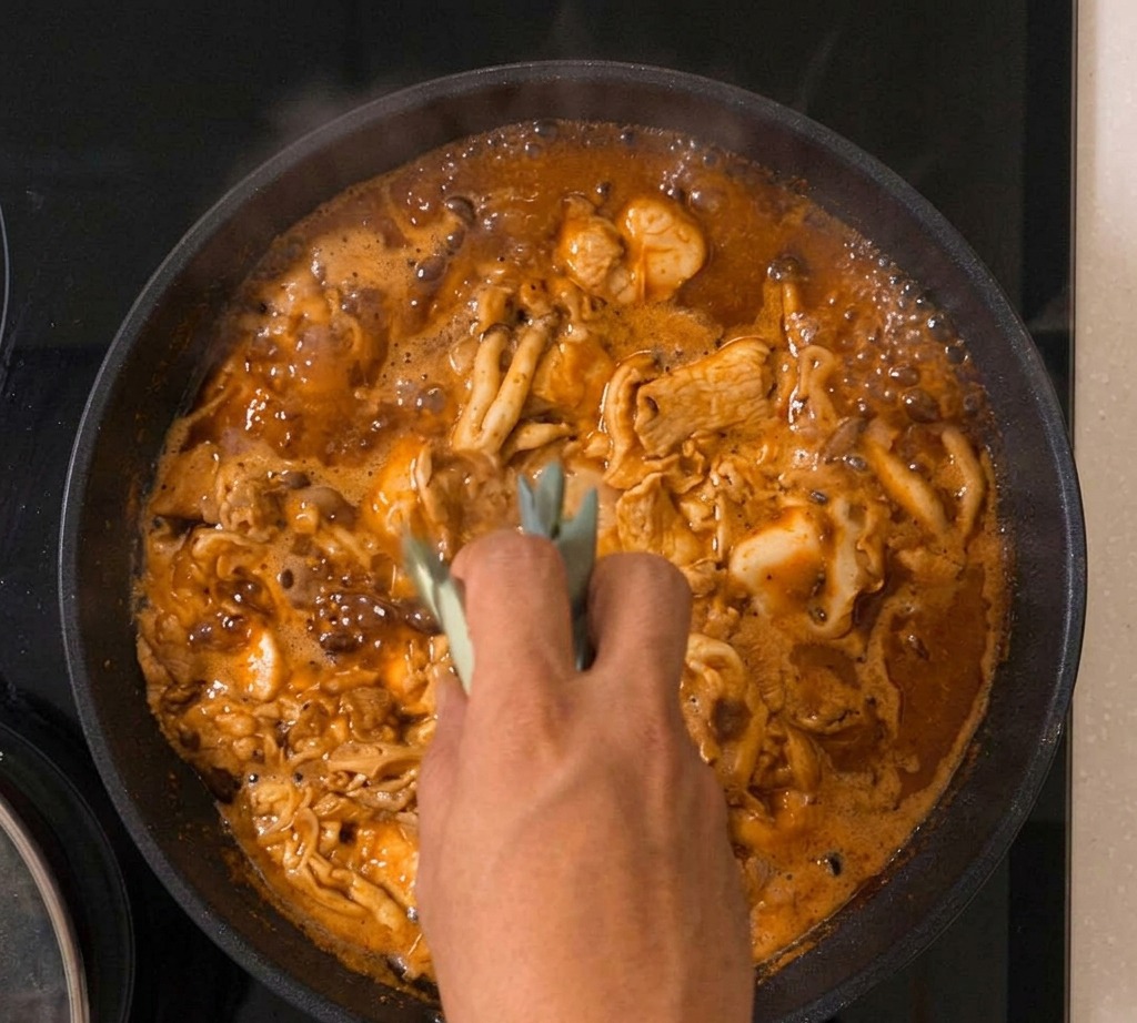 Il composto per lOyakodon che sobbolle in padella con cipollotti visibili tra luovo che si rapprende e il pollo.