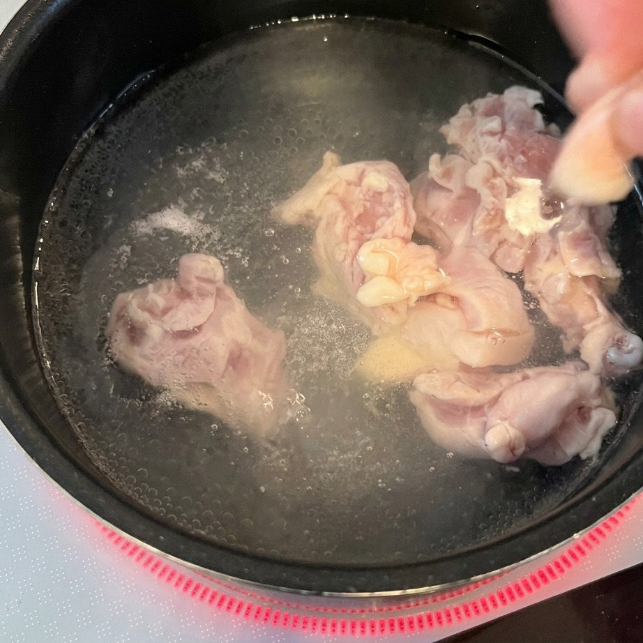 Bocconcini di pollo crudo immersi in una pentola dacqua bollente su un piano a induzione.