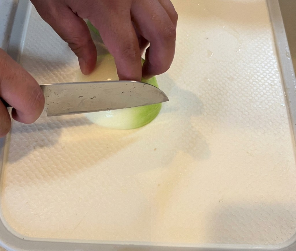 Una cipolla bianca tagliata a fette sottili su un tagliere bianco.
