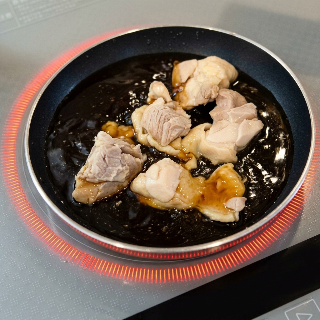 Pezzi di pollo sbollentati che sobbollono in una salsa marrone scuro in una piccola padella rotonda.