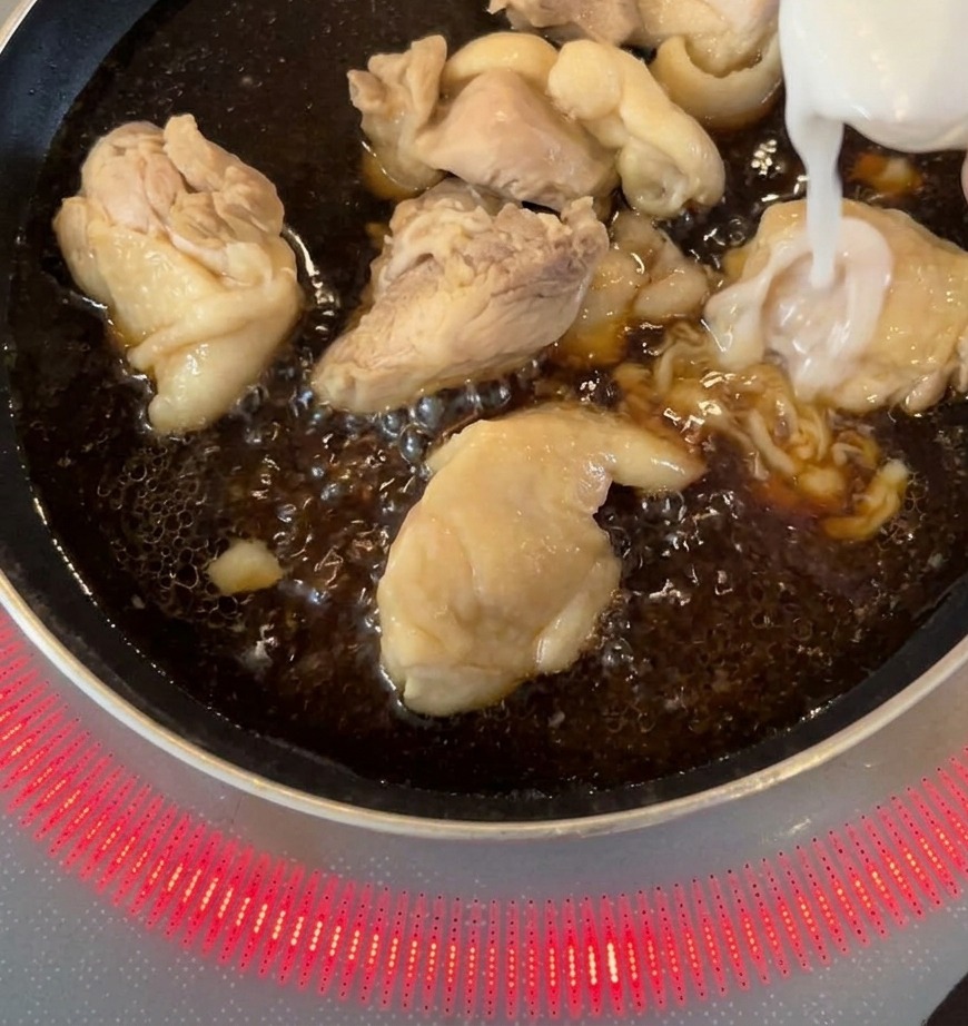 Cipolle bianche affettate aggiunte in padella con i pezzi di pollo che sobbollono in una salsa scura.