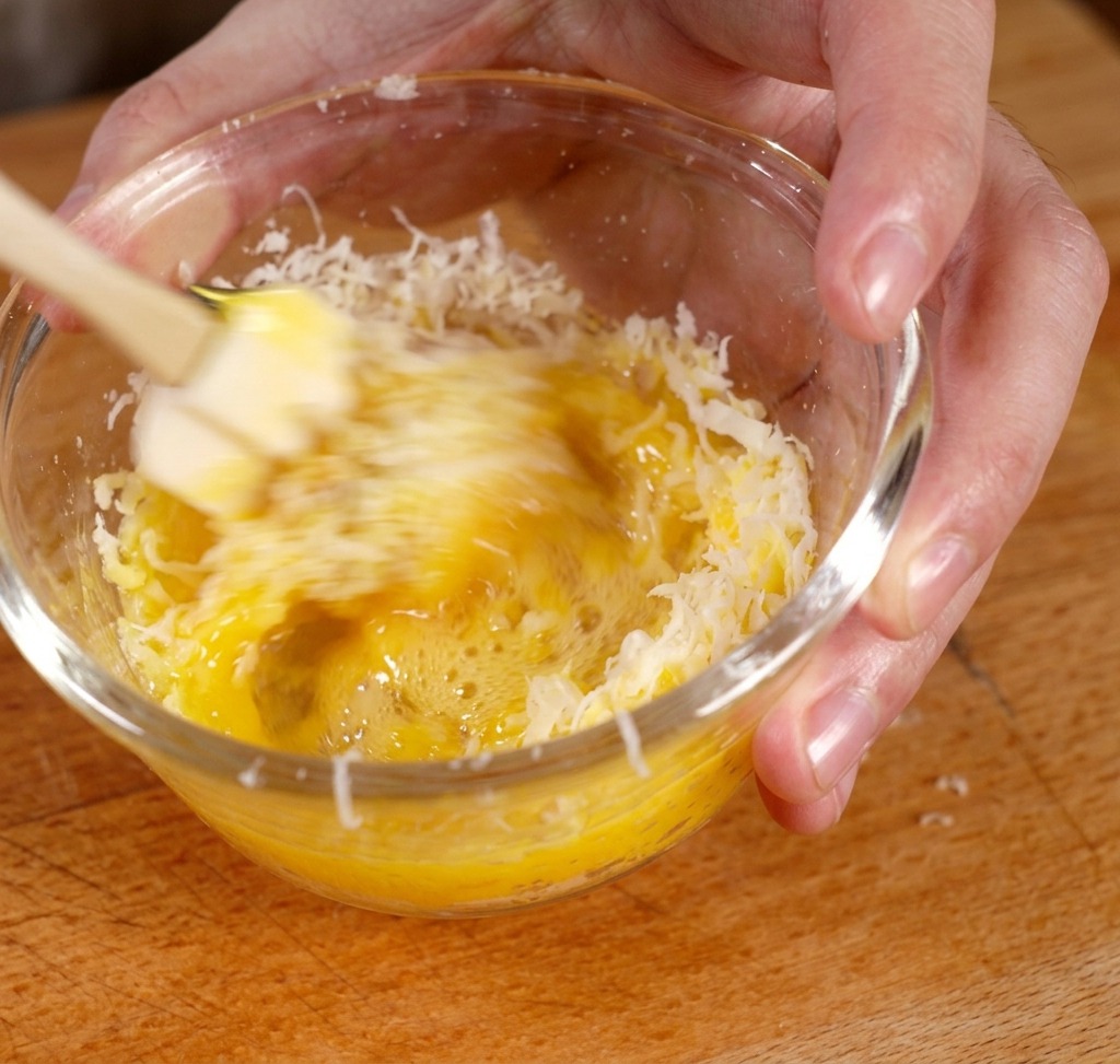 Mescolare tuorlo e parmigiano in una ciotola di vetro per formare una pasta gialla densa.