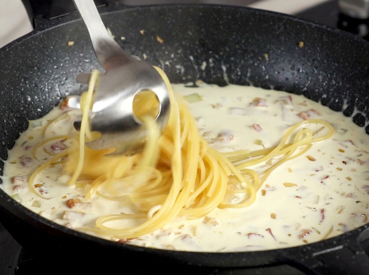 Spaghetti sollevati con un prendispaghetti e trasferiti nella salsa cremosa alla pancetta.