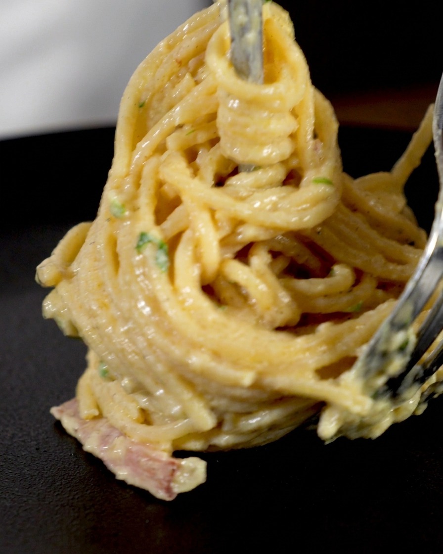 Spaghetti cremosi arrotolati attorno a un forchettone per formare un nido verticale perfetto.