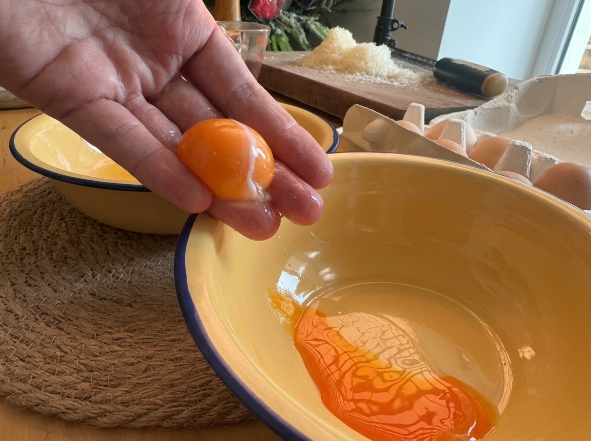 Una mano che separa un tuorlo duovo arancione vivo sopra una ciotola smaltata gialla.