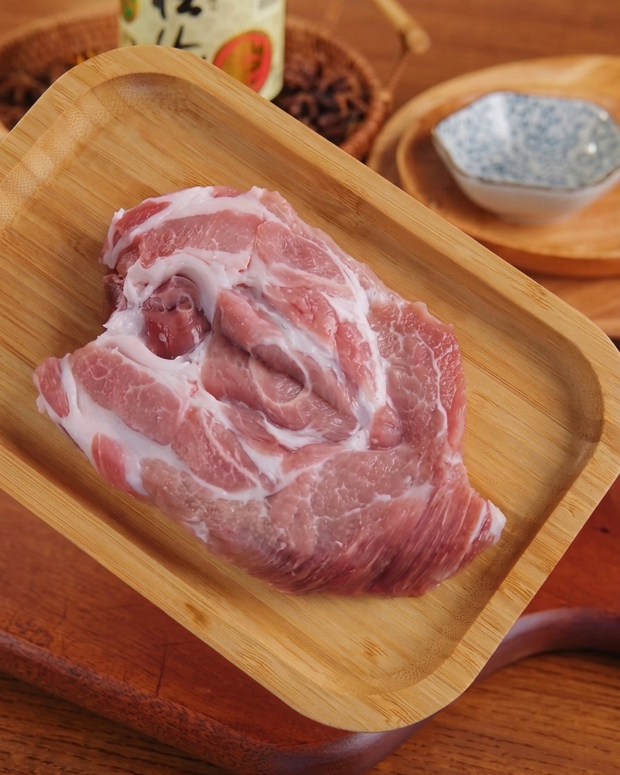 Una fetta di maiale marmorizzato crudo stesa su un tagliere di legno dopo essere stata battuta.