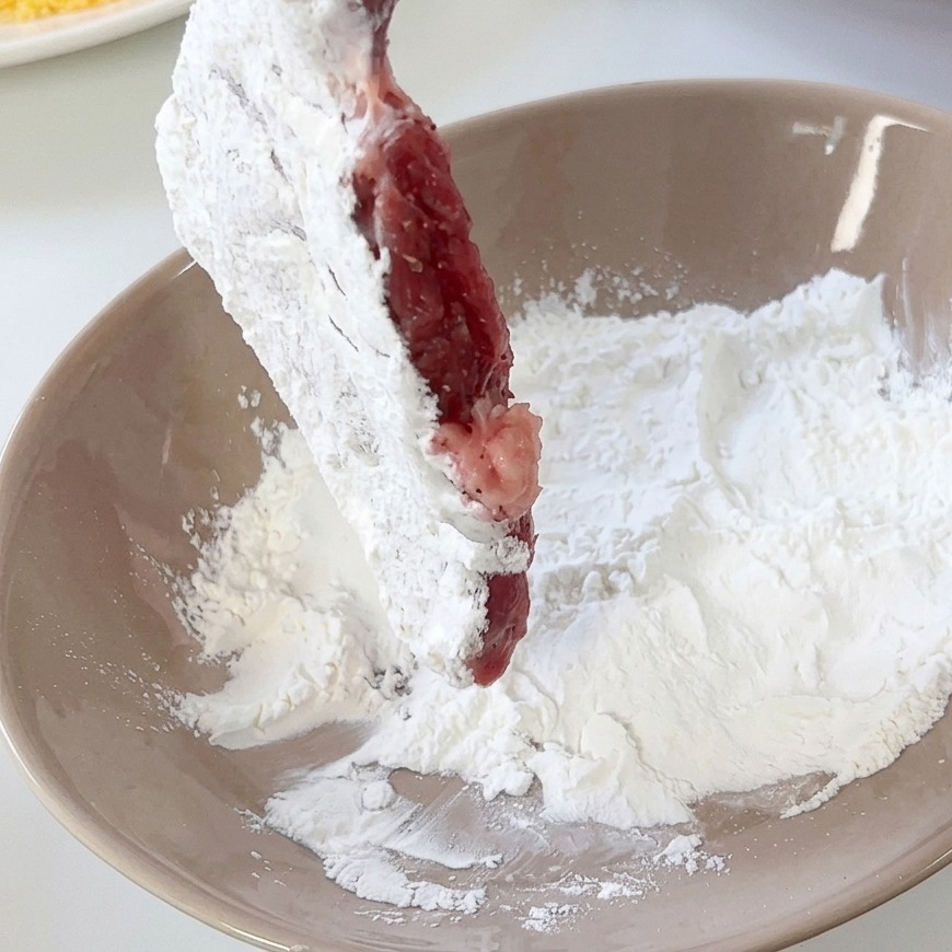 Una cotoletta di maiale infarinata allinterno di una ciotola di ceramica beige.