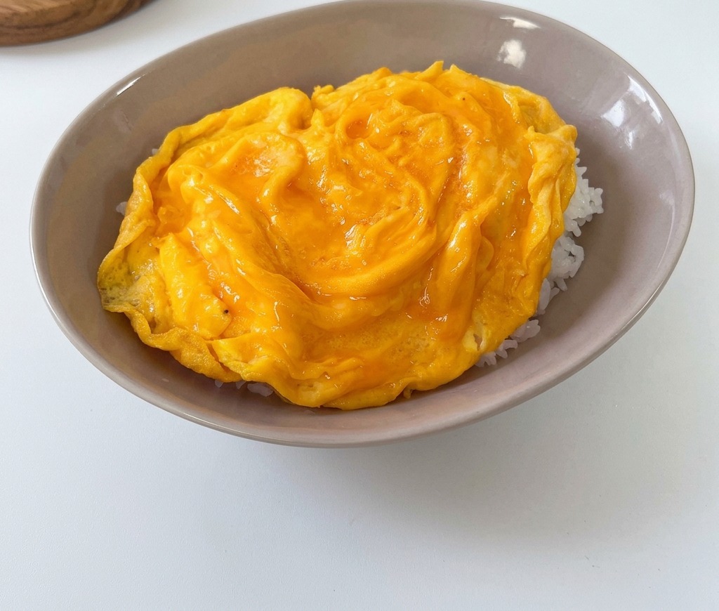 Una frittata gialla, soffice e cotta morbidamente, adagiata sopra un letto di riso bianco in una ciotola grigia poco profonda.