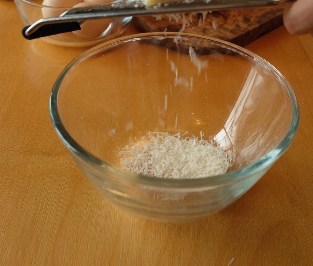 Un pezzo di Pecorino Romano grattugiato finemente in una ciotola di vetro.