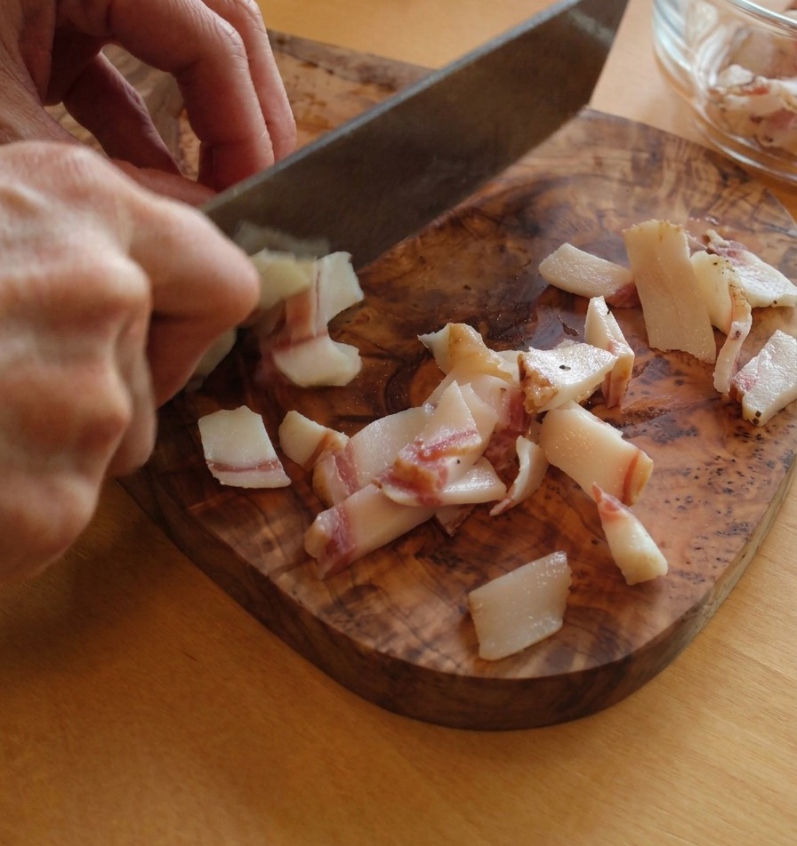 Taglio del guanciale a strisce rettangolari su un tagliere, mostrando gli strati di grasso e carne.