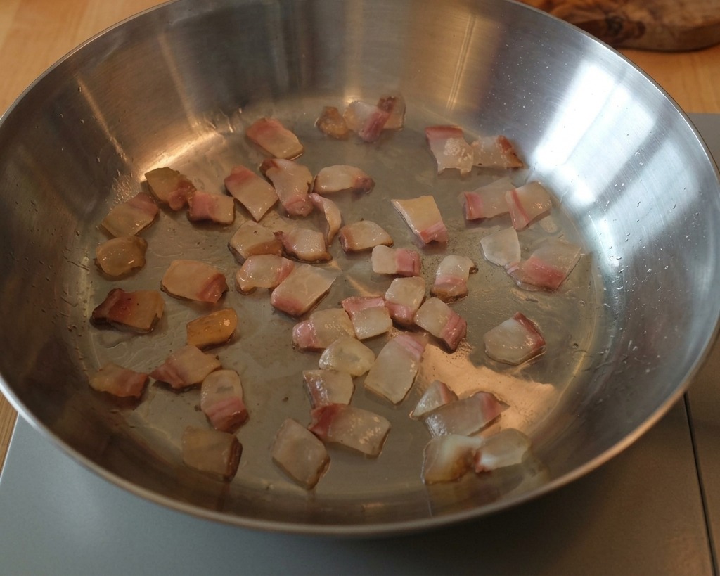 Cubetti di guanciale che rosolano in una padella di acciaio, con il grasso che diventa liquido.