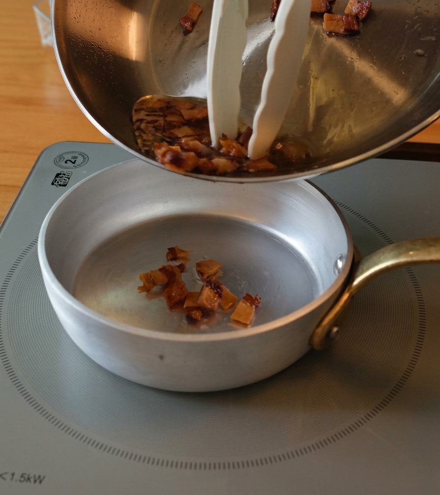 Travaso dei pezzetti di guanciale dorati e del grasso liquido in una ciotolina di preparazione.