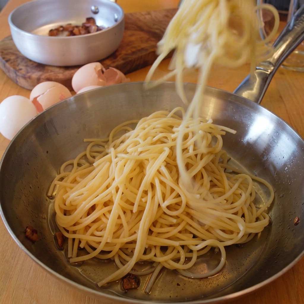 Pinze che versano spaghetti appena cotti nella padella di acciaio unta di grasso di guanciale.