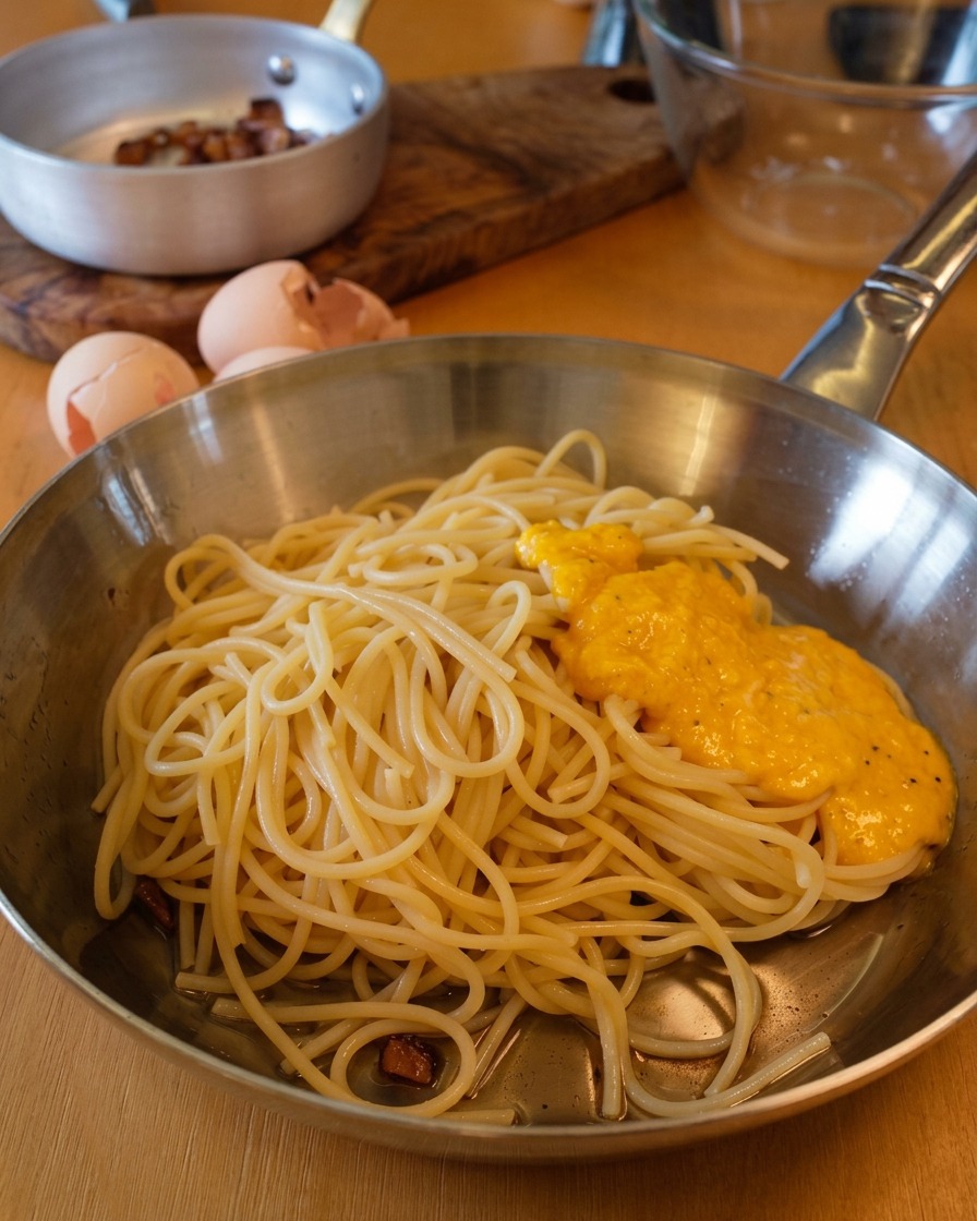 Una crema densa e dorata versata sopra una montagna di spaghetti in padella.