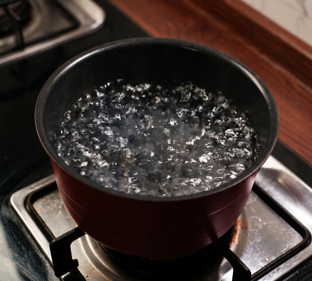 Una pentola rosso scuro su un fornello a gas piena dacqua che bolle con vapore che sale.